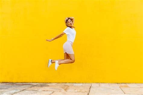 Premium Photo Cheerful Woman Jumping Against Yellow Wall