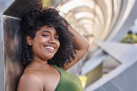 Latina sonriente con el pelo rizado en la ciudad mujer joven tocándose el pelo con la mano