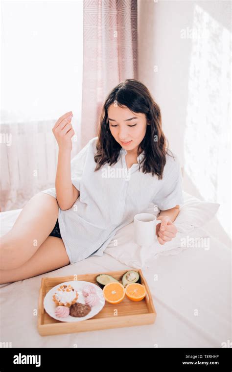 Indoor Photo Of Cute Shy Brunette Girl With Happy Smile Lying On Bed Near Window With Cup Of Tea