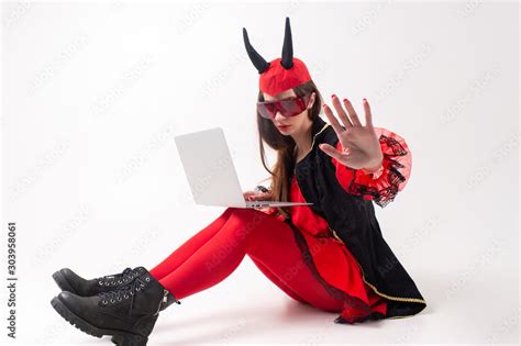 Sexy Brunette Woman In Red Tights Black Boots And Devil Horns Using Laptop Over White Studio