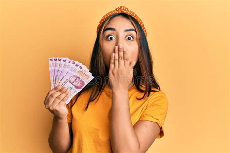 Joven Latina Sosteniendo Billetes De Pesos Mexicanos Cubriendo Boca Con Mano Impactada Y Con