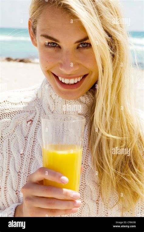 Female Very Long Blonde Hair Wearing Cream Knitted Jumper Holding Glass Of Orange Juice One Hand