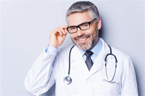 médecin expérimenté et confiant joyeux médecin mature ajustant ses lunettes et souriant en se