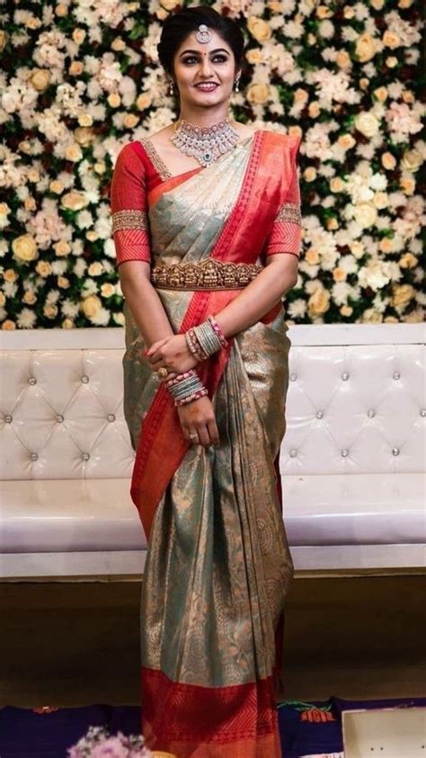 A Woman In A Red And Gold Sari Standing Next To A Floral Wall With Flowers