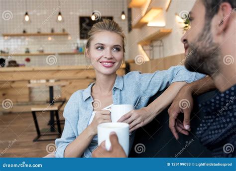 Happy Young Couple Holding Cups And Smiling Each Other While Sitting