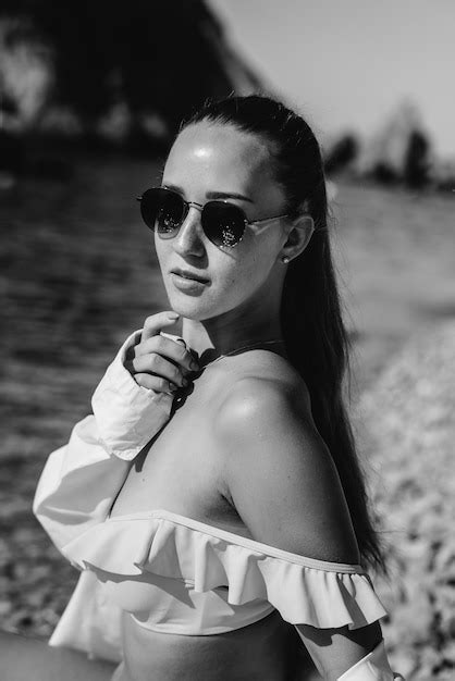 Una hermosa mujer joven con gafas y bikini está sentada en la orilla del mar con el telón de