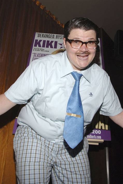 A Man Wearing Glasses And A Blue Tie Posing For A Photo In Front Of A Sign