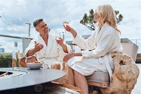 Beautiful Mature Couple In Bathrobes Enjoying Fruits And Wine While Relaxing In Luxury Hotel