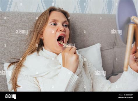 Attraktive blonde Frau überprüft ihre Kehle mit Holzstab und Spiegel liegen im Bett und fühlen