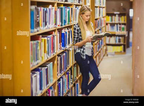 Blonde Student Reading Book Next To Bookshelf Stock Photo Alamy