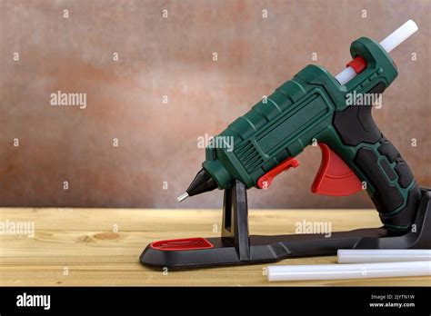 Electric Hot Glue Gun With Stand And White Glue Sticks On Wooden Background Selective Fokus