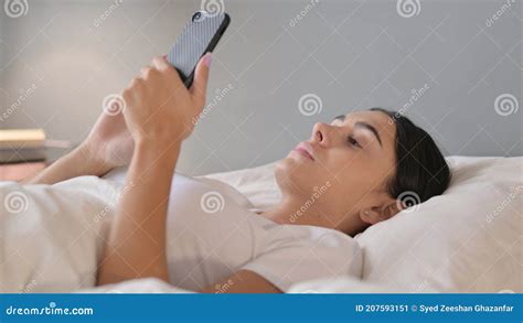 Mujer Latina Usando Smartphone En La Cama Imagen De Archivo Imagen De