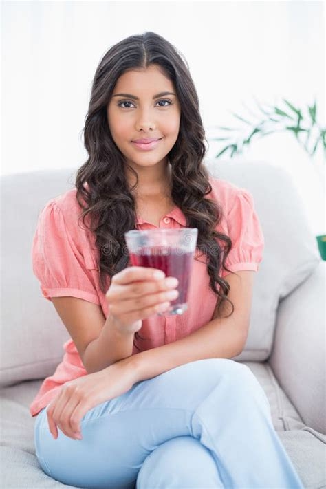 Content Cute Brunette Sitting On Couch Holding Glass Of Juice Stock