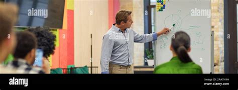Confident Mature Coach Or Speaker Pointing At Flip Chart And Explaining
