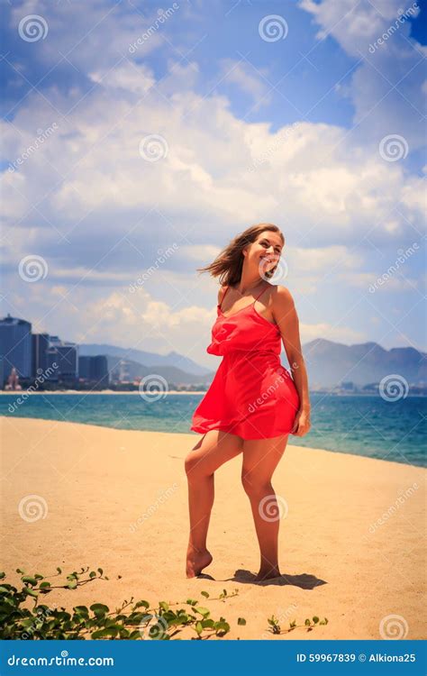 La Fille Blonde En Rouge Danse Nu Pieds Sur Cheveux De Secousses De Vent De Sable De Longs Image