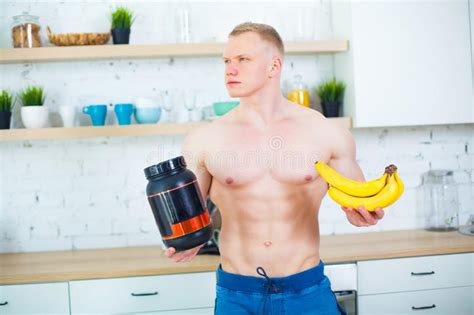 Muscular Man With A Naked Torso In The Kitchen With A Sports Nutrition Protein And Bananas The