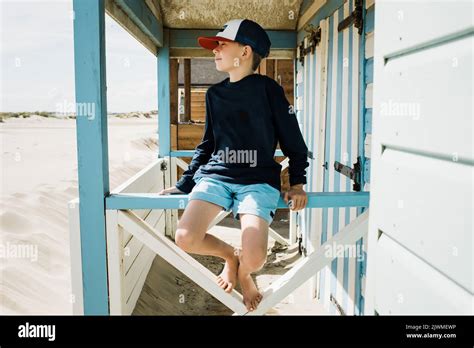 boy sat on a beach hut casually looking across the beach for surf Stock ...
