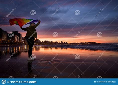 Asombrosa Foto De Un Joven Parado En La Playa Y Sosteniendo En Las Manos Una Bandera Gay Imagen