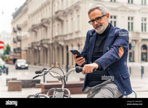 Modern Bearded Grey Haired Mature Man Using His Smartphone And Riding A