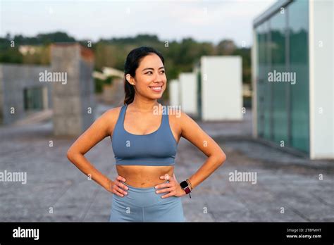 A Latina Woman In Workout Gear Rests Her Hands On Her Hips Smiling Confidently During An