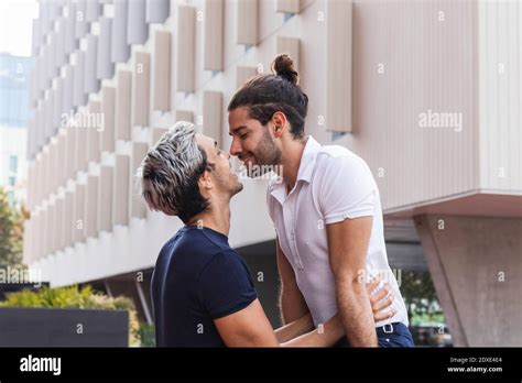 Homme souriant regardant le partenaire gay tout en s embrassant contre le bâtiment en ville
