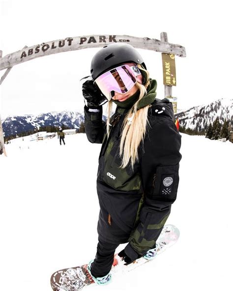 A Woman Standing On Top Of A Snowboard Under A Sign That Says Absolut Park