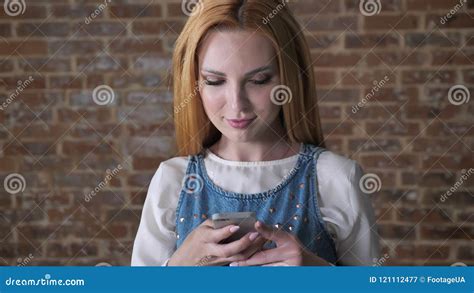 Le Jeune Attirant La Fille Blonde Introduit Le Message Sur Le Smartphone Fond De Brique