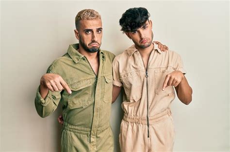 Homosexual Gay Couple Standing Together Wearing Casual Jumpsuit Pointing Down Looking Sad And