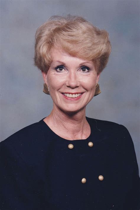 An Older Woman With Blonde Hair Smiling At The Camera In Front Of A Gray Background