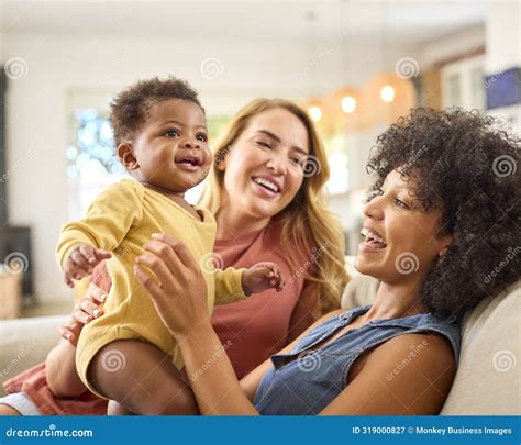 Same Sex Female Couple Or Friends Playing With Baby Sitting On Sofa At Home Together Stock Image