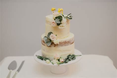 A Three Tiered Cake With Flowers And Greenery Sits On A Table Next To