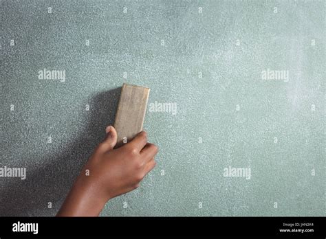 Cropped Hand Of Student Holding Duster On Blackboard In Classroom Stock