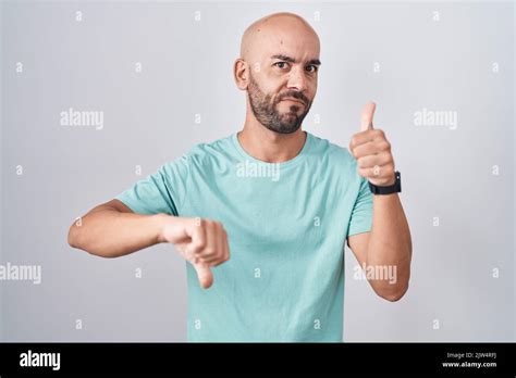 Middle Age Bald Man Standing Over White Background Doing Thumbs Up And Down Disagreement And