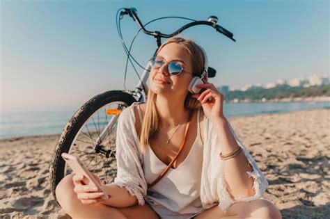 Élégante jeune femme souriante blonde séduisante assise sur la plage avec vélo dans les