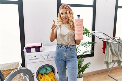 Beautiful Blonde Woman Doing Laundry Holding Detergent Bottle Smiling Happy And Positive Thumb