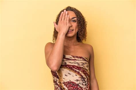Joven mujer transexual latina aislada de fondo amarillo divirtiéndose cubriendo la mitad de la