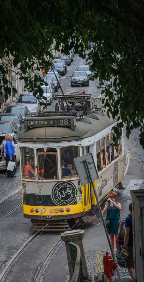 A Yellow And Green Trolly Car Traveling Down A Street Next To People