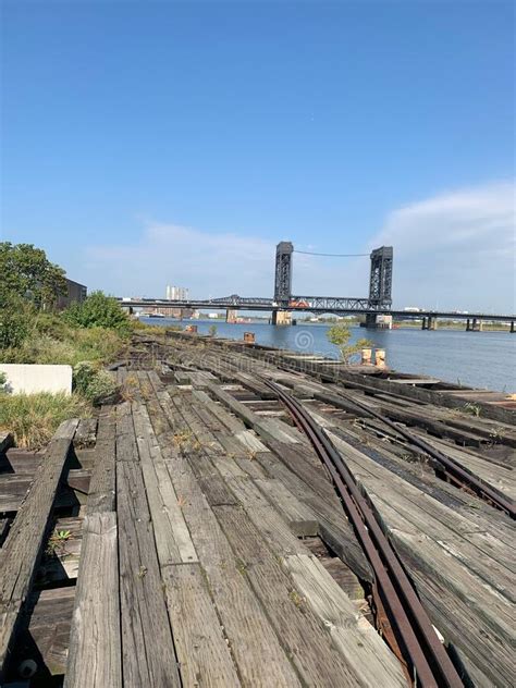 Old And Worn Train Tracks By The Water With A Bridge In The Background
