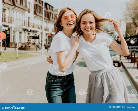 Twee Jonge Glimlachende Hipster Blonde Vrouwen In Kleren Van De De Zomer De Witte T Shirt Stock