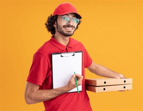 Joyeux Jeune Livreur Caucasien En Uniforme Rouge Et Casquette Portant