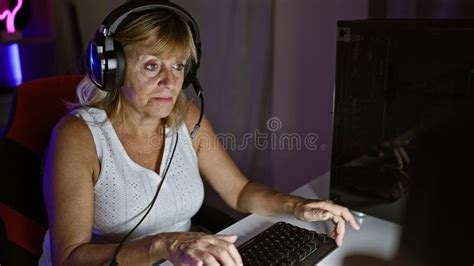 Beautiful Middle Age Blonde Woman Streamer Seriously Immersed Wearing Headphones Playing Video