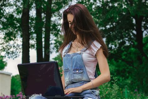 Junger Netter Brunette Mit Dem Langen Haar Das In Einem Park Mit Einem Laptop Sitzt Stockbild