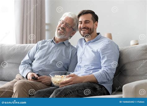 Happy Mature Father And Son Watching Tv Show Together Stock Photo