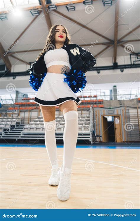 Bottom View Vertical Shot Of Brunette Cheerleader Posing With Blue Shiny Pom Poms Basketball