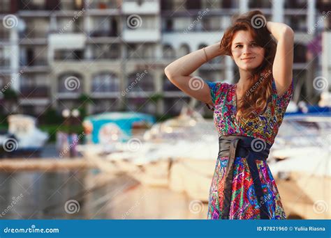 Attractive Brunette In Long Colorful Dress Standing Alone On The Beach Against The Backdrop Of
