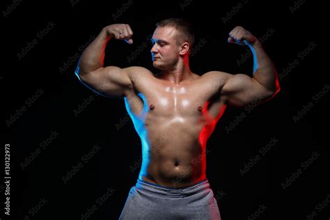 Male Bodybuilder Athlete With Naked Torso Posing Against A Black Background In Red And Blue
