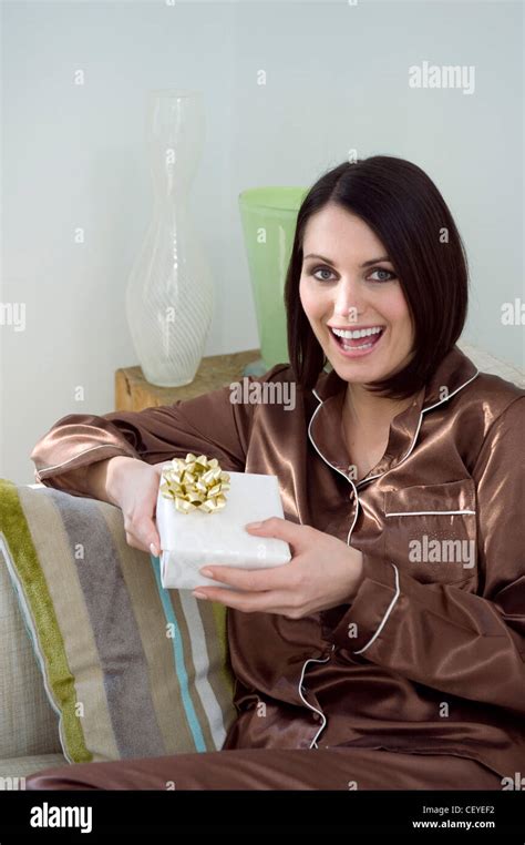 Female Shoulder Length Brunette Hair Wearing Brown Satin Pyjamas Sitting On The Sofa Holding A