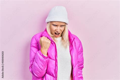 Beautiful Caucasian Blonde Woman Wearing Wool Hat And Winter Coat Angry And Mad Raising Fist
