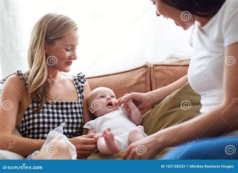 Loving Female Same Sex Couple Cuddling Baby Daughter On Sofa At Home Together Stock Image
