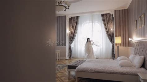 Bride In Lingerie Dancing With Her Wedding Dress At Home Near Window White Boudoir Dress And